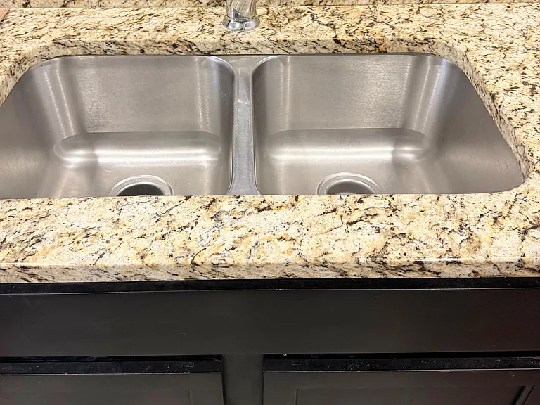Kitchen workspace with a double-basin stainless-steel sink, pull-out faucet, and granite-look countertops for meal prep.