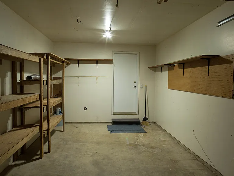 Attached garage with oversized storage/workshop area, built-in shelving, and direct interior access to the home through the corridor leading to the kitchen and living room.