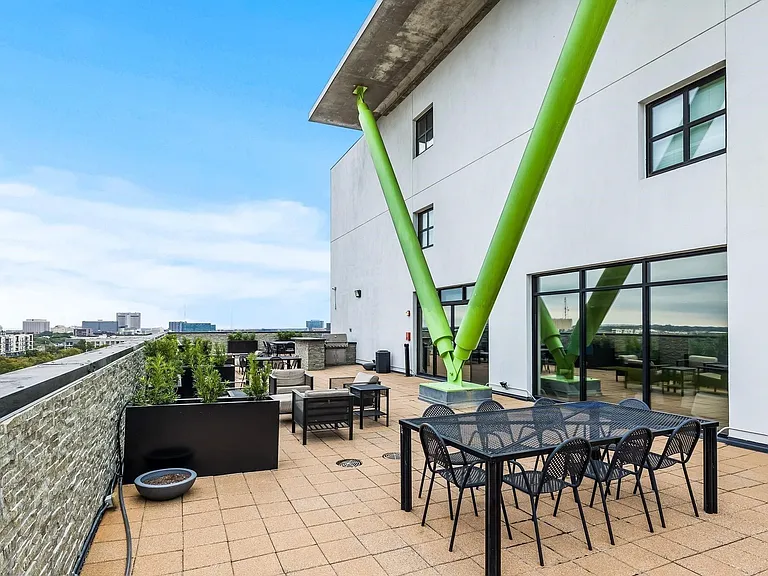 Expansive outdoor patio featuring square tile flooring, a stone-clad perimeter wall, multiple seating areas, and a visible city skyline