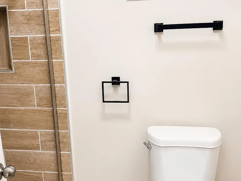 Clean bathroom with a glass-enclosed tiled shower, window for ventilation, and updated matte-black fixtures.