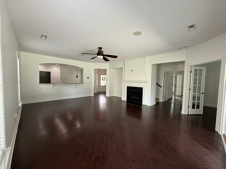 Bright, open-concept living room featuring gleaming dark hardwood floors, a cozy fireplace, and a striking arched cutout with a breakfast bar looking into the kitchen