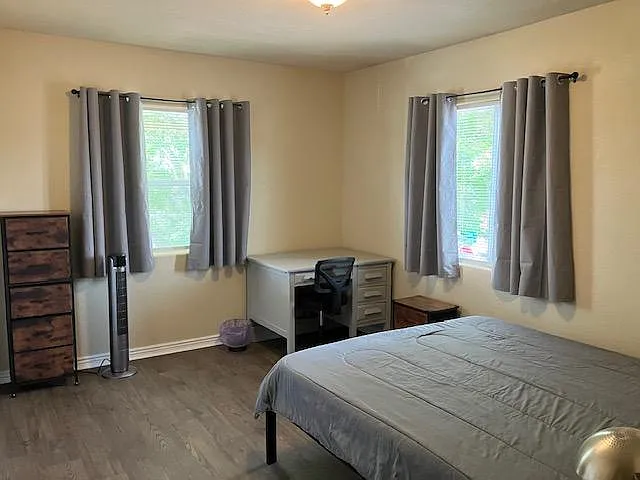 Furnished bedroom with two windows, a work desk, dresser storage, and durable hard-surface flooring.