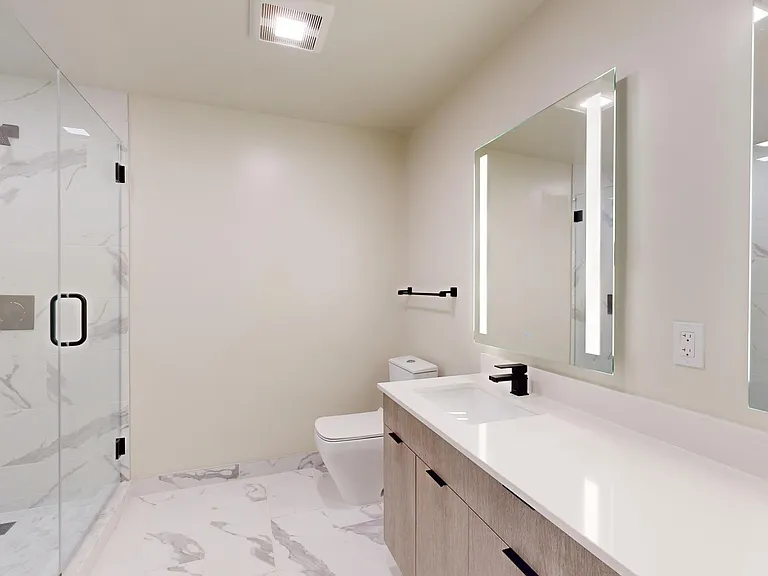 Apartment bathroom with glass-enclosed shower, tile flooring, and LED vanity mirror.