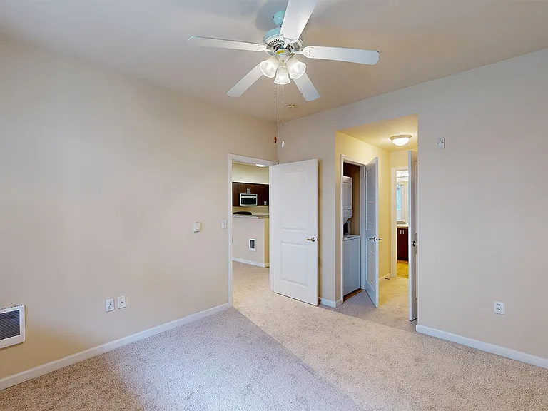 Spacious apartment bedroom with large closet, attached bathroom and plush carpet flooring.