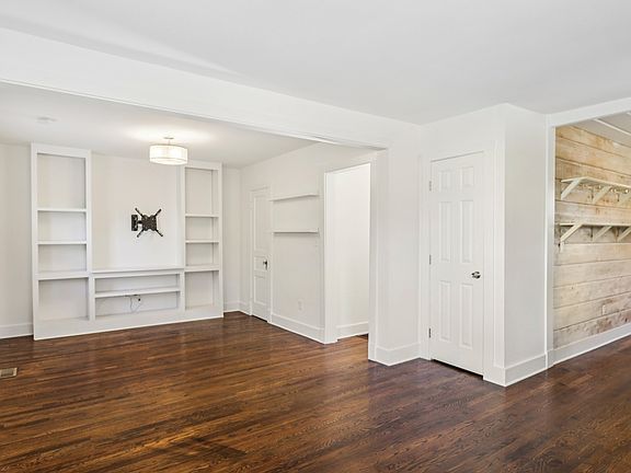Bright main living space with hardwood floors, built-in shelving, and fresh paint. The large windows bring in abundant natural light.