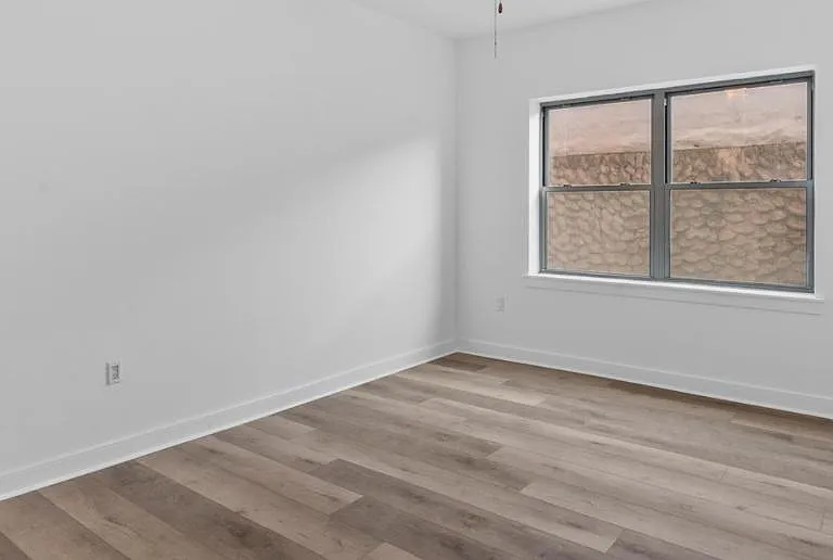 Unfurnished bedroom with wood-look flooring, smooth white walls, and a large window for natural light and fresh air.