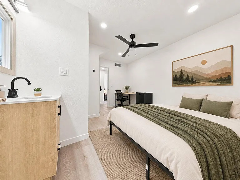 Spacious bedroom with ceiling fan, private sink/vanity, and a dedicated desk nook plus mini fridge for daily convenience.