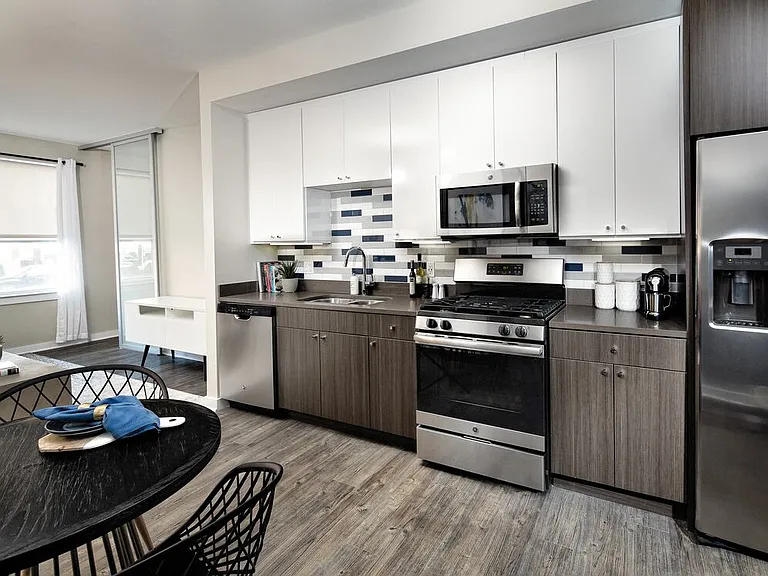 Modern Package kitchen with white and dark brown cabinetry, dark grey granite countertops, multi-colored subway tile backsplash, stainless steel appliances, and hard surface flooring