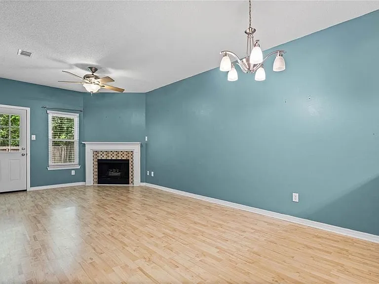 Spacious room featuring wood-finish flooring, a fireplace with a tiled surround, a white mantel, and a ceiling fan