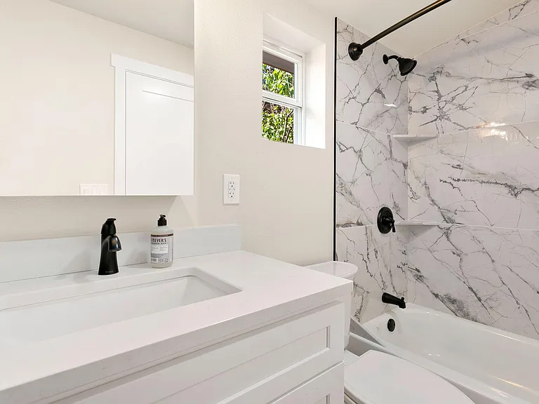 Updated bathroom with a wide vanity, matte-black fixtures, and a tub/shower surround with marble-look tile.