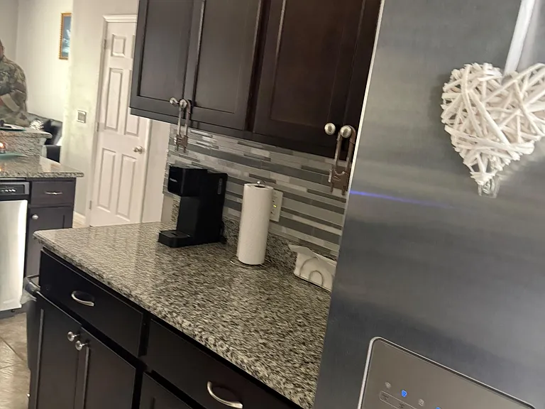 Kitchen features dark cabinetry, granite-look counters, tile backsplash, and a refrigerator with in-door water/ice.