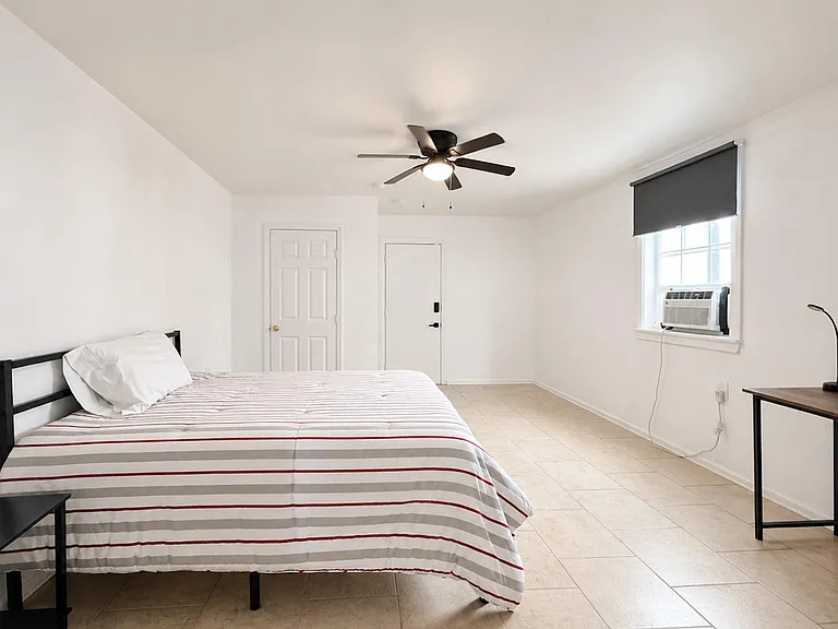 Spacious bedroom with tile flooring, ceiling fan, and a window A/C unit for comfort, plus room for a desk or seating.