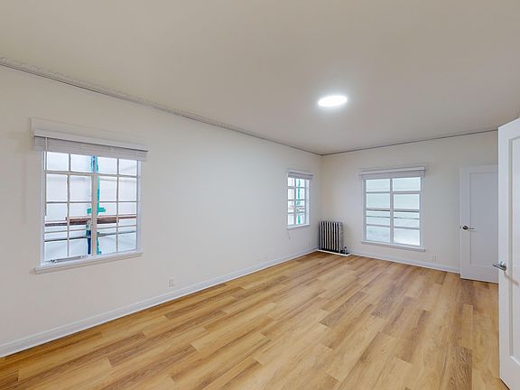 Bright room with wooden flooring, two windows with blinds and a radiator against a plain wall