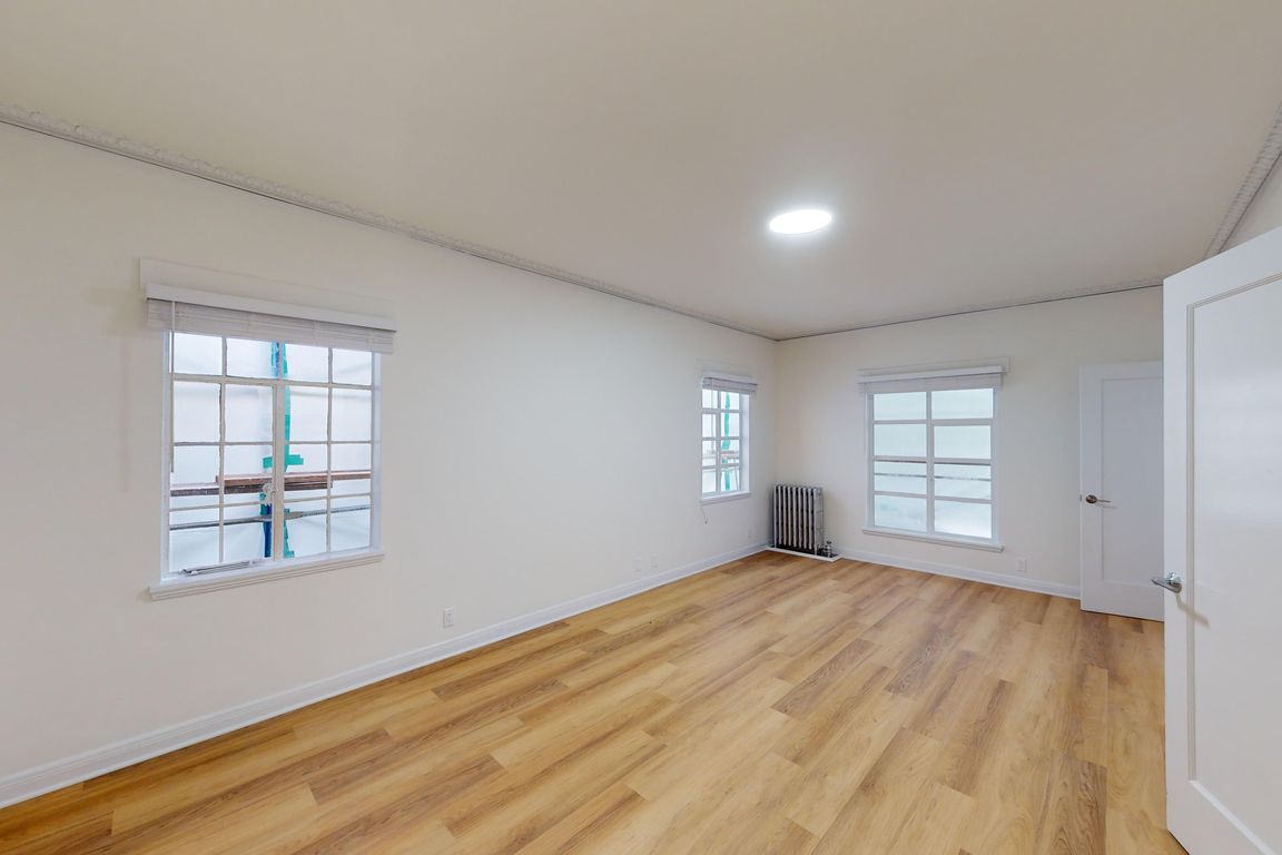 Bright room with wooden flooring, two windows with blinds and a radiator against a plain wall
