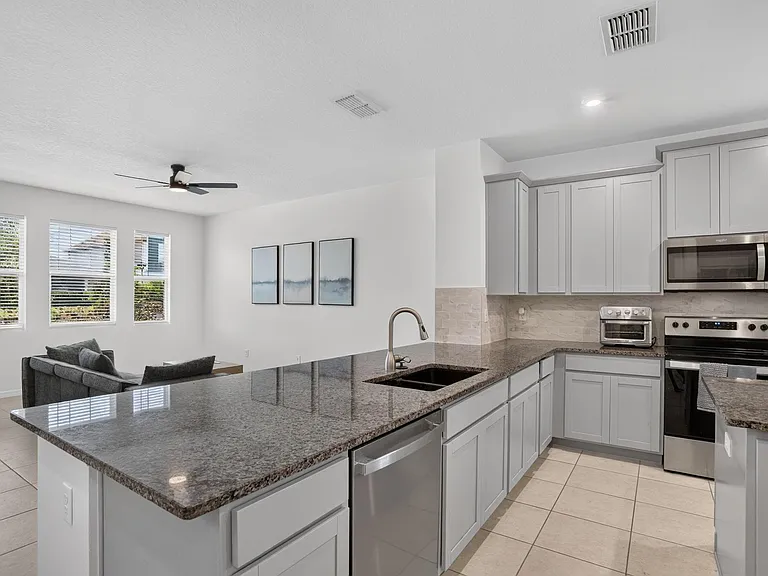 Open kitchen with granite counters, ample cabinetry, stainless appliances, and a breakfast bar overlooking the living area.