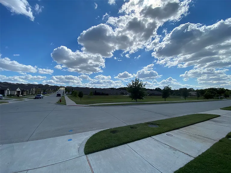 Neighborhood street featuring concrete sidewalks and manicured green spaces