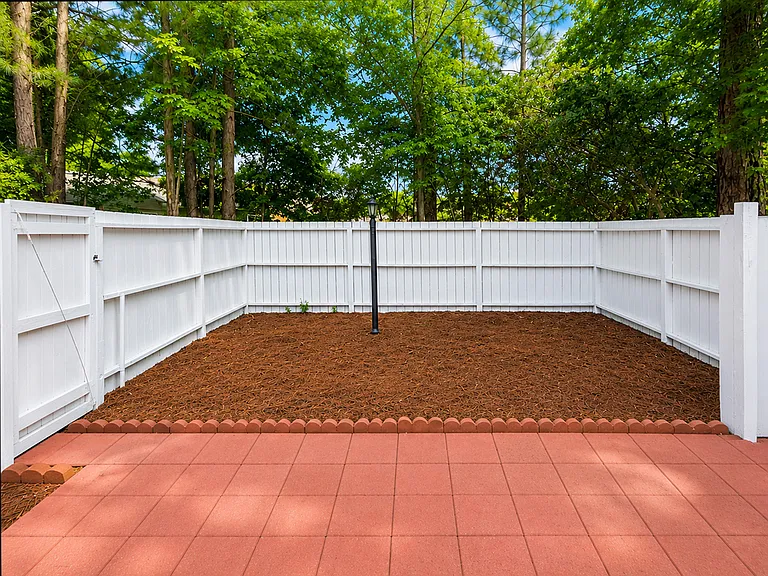 Backyard with mulch, brick tile, fence, & lamp post.
