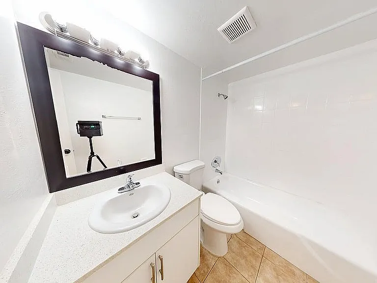 Bright and modern bathroom featuring a sleek vanity, spacious mirror, and pristine white bathtub.