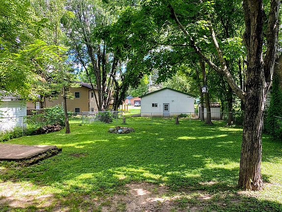 Large fenced in backyard with stone fire ring.