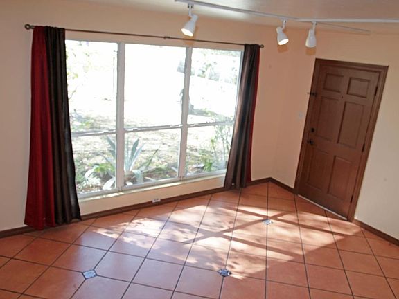 The entrance door and a possible living room. Large room , extra large window and tile floor. Track lighting. Room connects to the kitchen with semi open space.