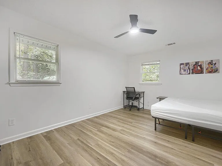 Spacious bedroom with two windows, ceiling fan, wood-look flooring, and room for a bed plus a dedicated desk area.