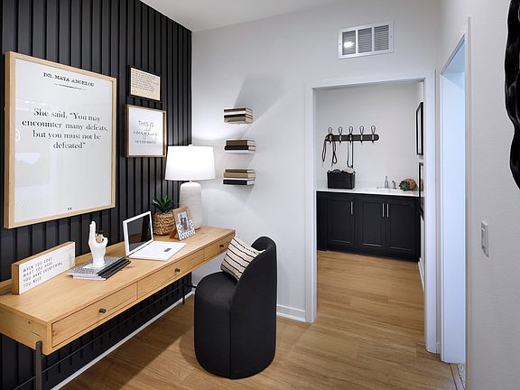 A modern and minimalist home office space with a wooden desk, black chairs, and a framed artwork on