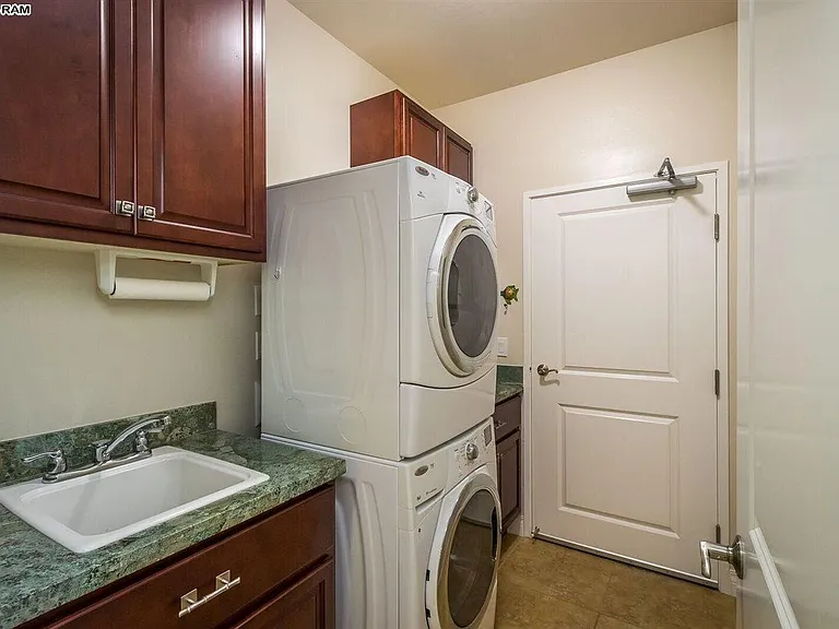 Laundry room with sink and storage cabinets. Stacked Maytag washer/dryer. Dyson vacuum. Door leads to garage.