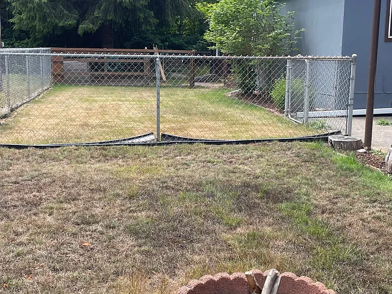 Left side of the fenced in yard with fire pit