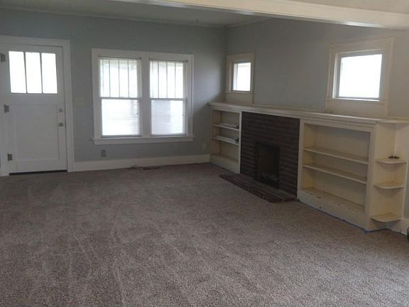 Living room with bookcase. Hand textured wall with light gray paint and white trim. New Carpet.