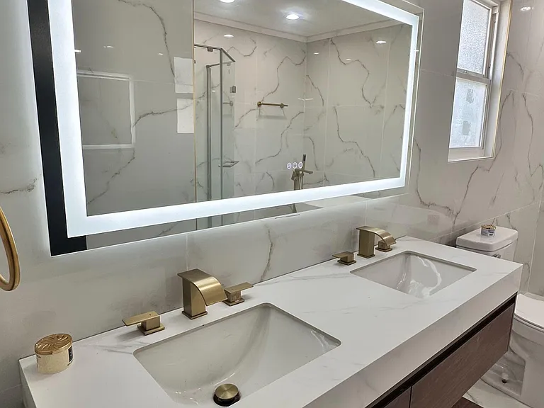 Renovated bath with double vanity, LED mirror, quartz-style countertop, and a window for added light and ventilation.