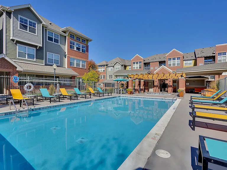 Inviting apartment community showcasing a sunlit pool area with colorful lounge chairs and modern building architecture.