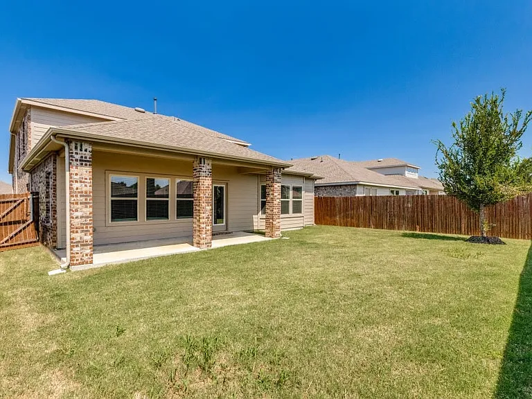 Expansive backyard featuring a covered patio with brick columns, a privacy fence, and a young tree