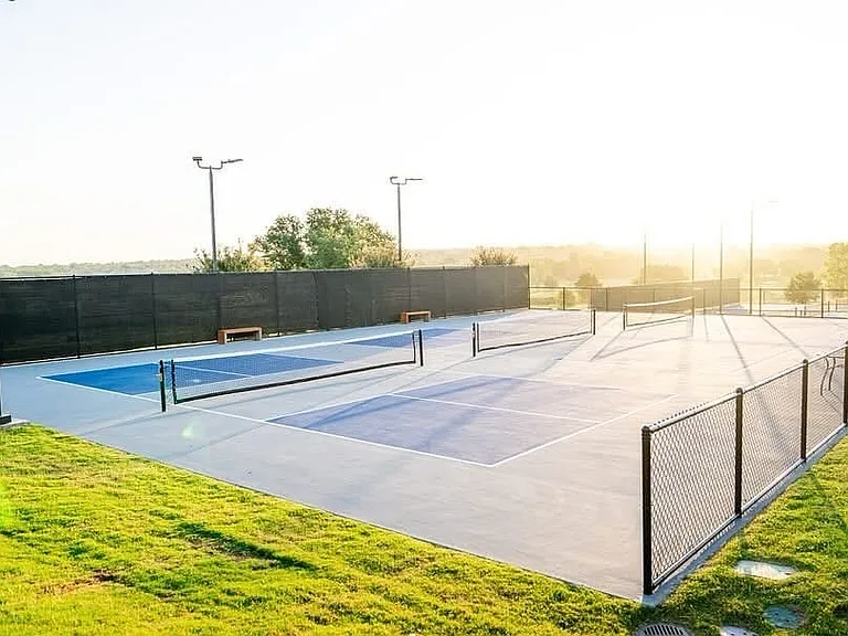 Multi-court facility featuring hard surface courts with painted blue and gray playing areas, perimeter fencing, and integrated lighting fixtures