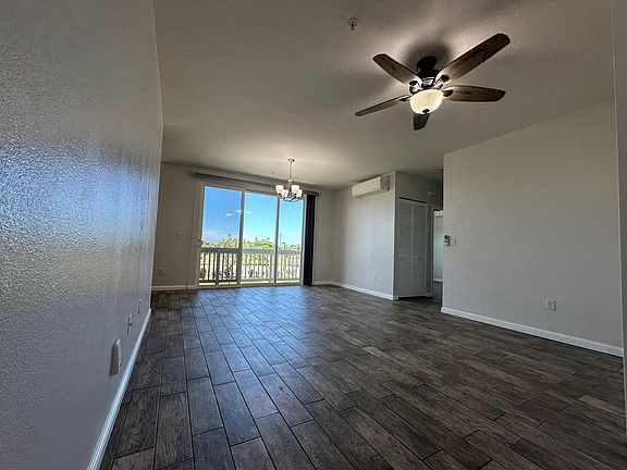 Spacious open-concept living and dining area with wood-look tile flooring, and abundant natural light from large sliding glass doors. Features include a ceiling fan, split A/C unit, and direct access to the kitchen, creating a versatile space