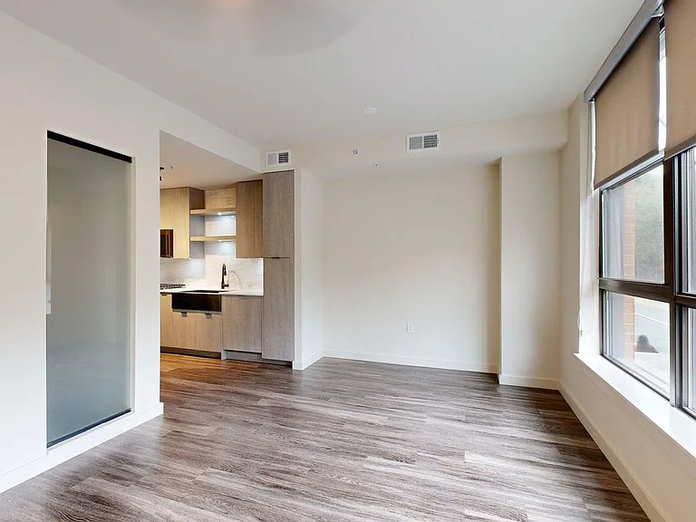 Apartment Kitchen with Stainless Steel Appliances, Dining and Living Room with wood flooring.