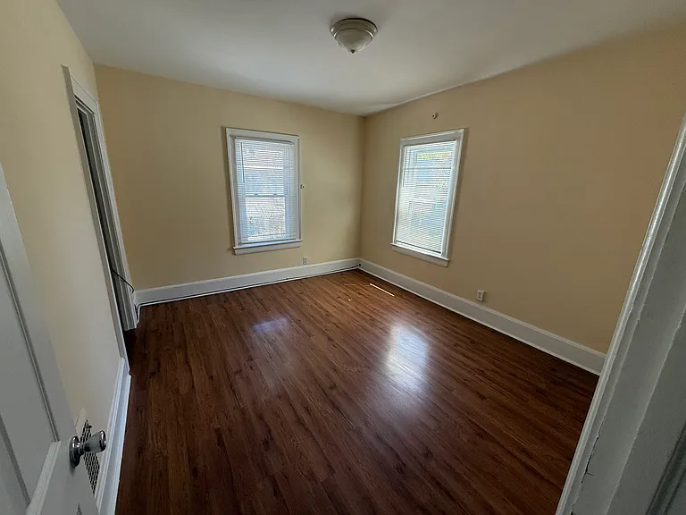 View of upstairs front bedroom, with windows facing forward (above the front porch) and right (looking down Luzerne Street). A closet is shown to the left. All walls and moulding painted in 2025. New door (2025).