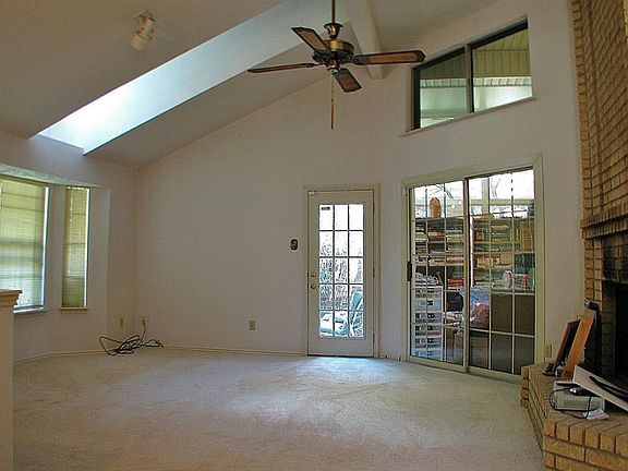 The living room has a fireplace and a high vaulted ceiling with a dormer and a ceiling fan. An enclosed sun porch is situated between the living room and the master bedroom.