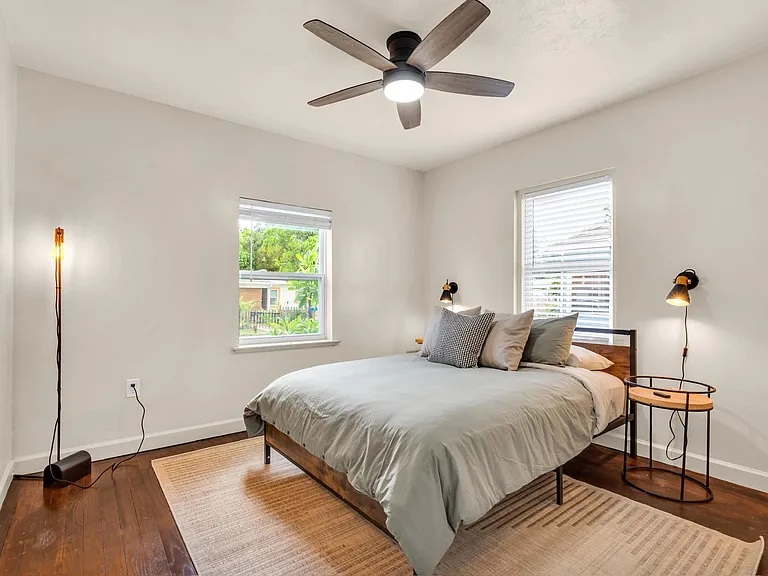Bedroom features a ceiling fan, hardwood floors, and two windows with blinds for natural light and privacy.