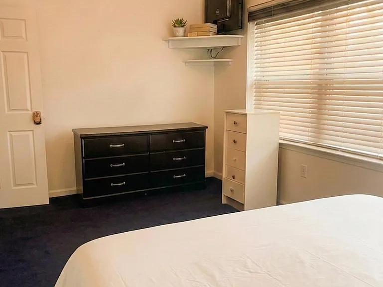 Furnished bedroom with a full bed, two dressers for storage, and a wide window with blinds for natural light.