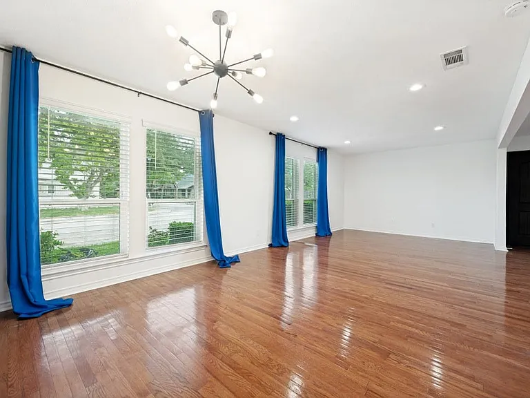 Spacious living area featuring polished wood flooring, multiple windows with blinds, a modern sputnik-style chandelier, recessed ceiling lighting, and crisp white walls
