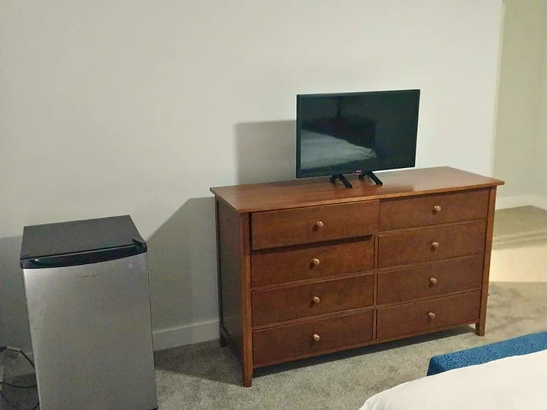 Large room for rent furnished with television, mini-fridge, and dresser.