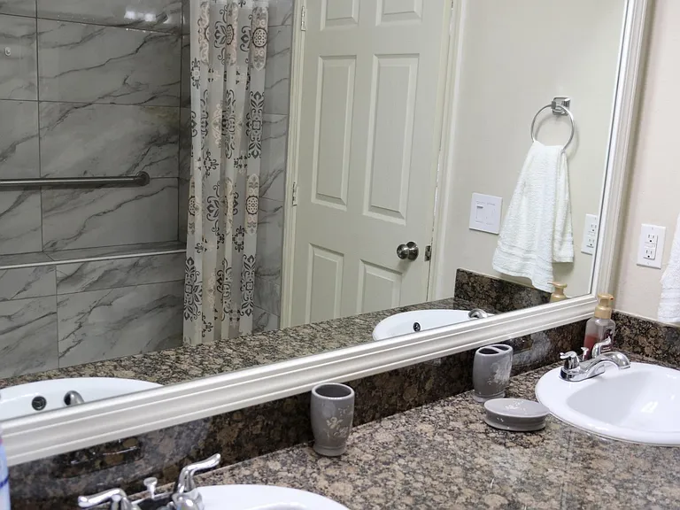 Full bathroom with a wide granite vanity, large framed mirror, and tiled tub/shower surround for easy daily routines.