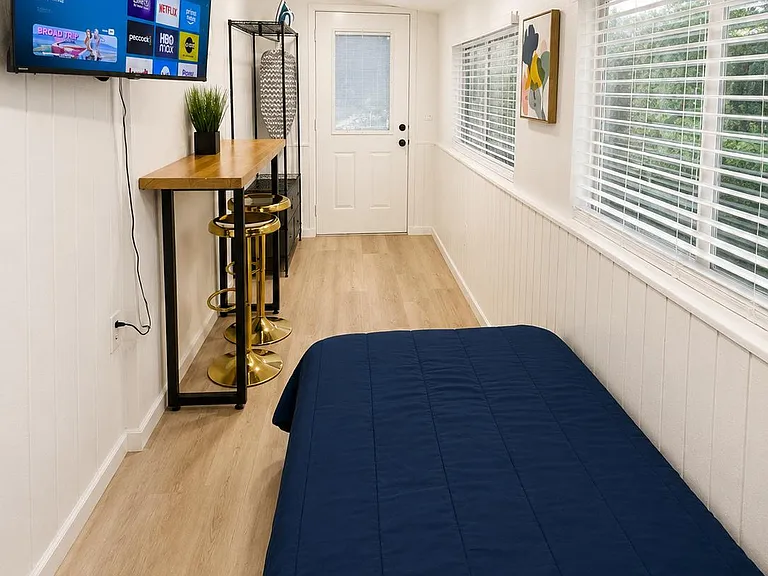 Sleeping area with a bed, wall-mounted TV, and a work bar with stools, plus large windows and easy outdoor access
