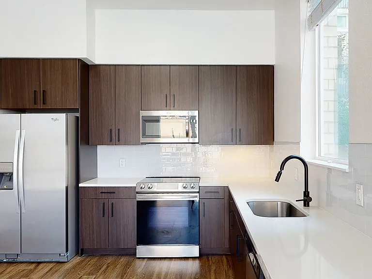 Apartment kitchen with stainless steel appliances, quartz countertops and wood-style flooring.