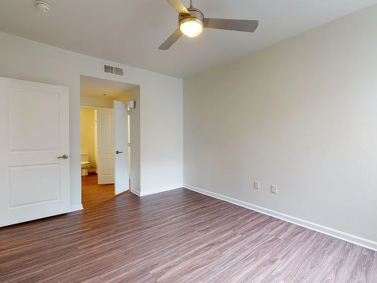 Spacious apartment bedroom with large closet, attached bathroom and wood-style flooring.
