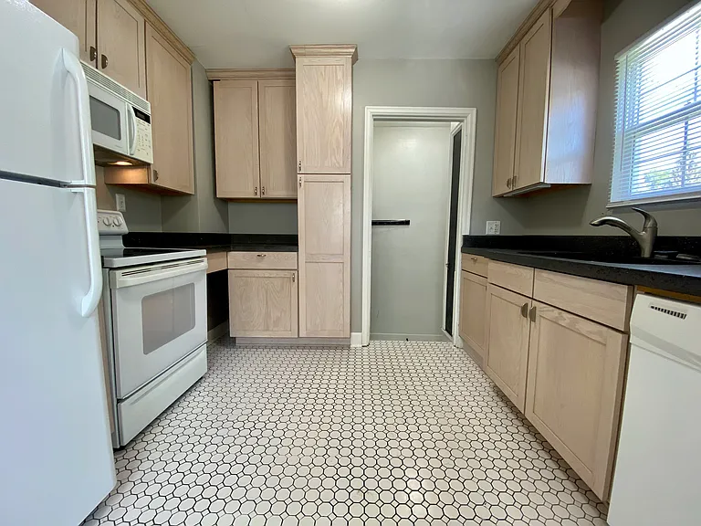 Charming kitchen with modern appliances, honey-colored cabinetry, and sleek black countertops, enhanced by natural light from a window. Charming kitchen with modern appliances, honey-colored cabinetry, and sleek black countertops, enhanced by natural ligh