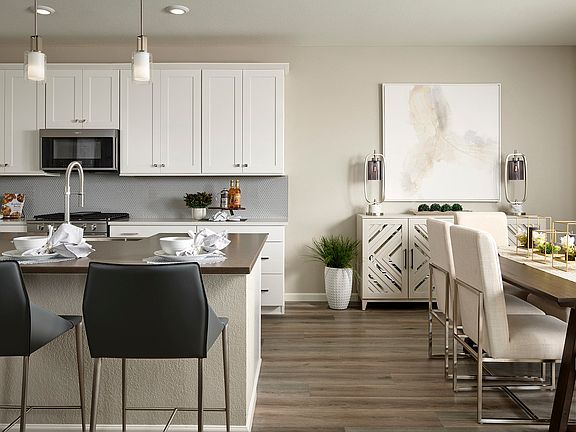 A modern and well-designed kitchen with white cabinets, a wooden dining table, and a cozy living are