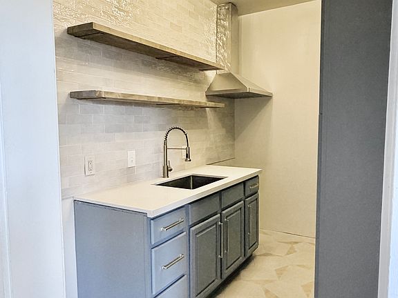 Newly remodeled kitchen with quartz countertop and butcher block floating shelves. Stainless steel fridge and electric range being delivered