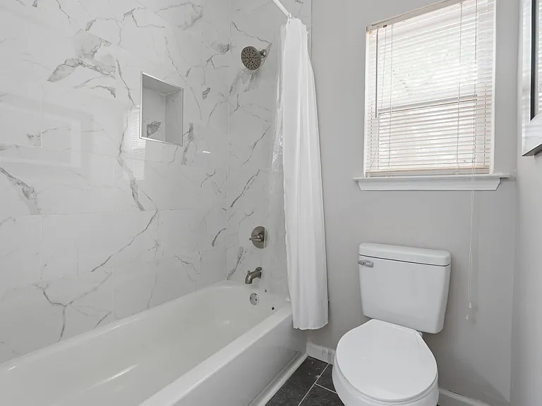 Updated full bath featuring a tiled tub/shower with built-in niche, chrome fixtures, and a window for ventilation.
