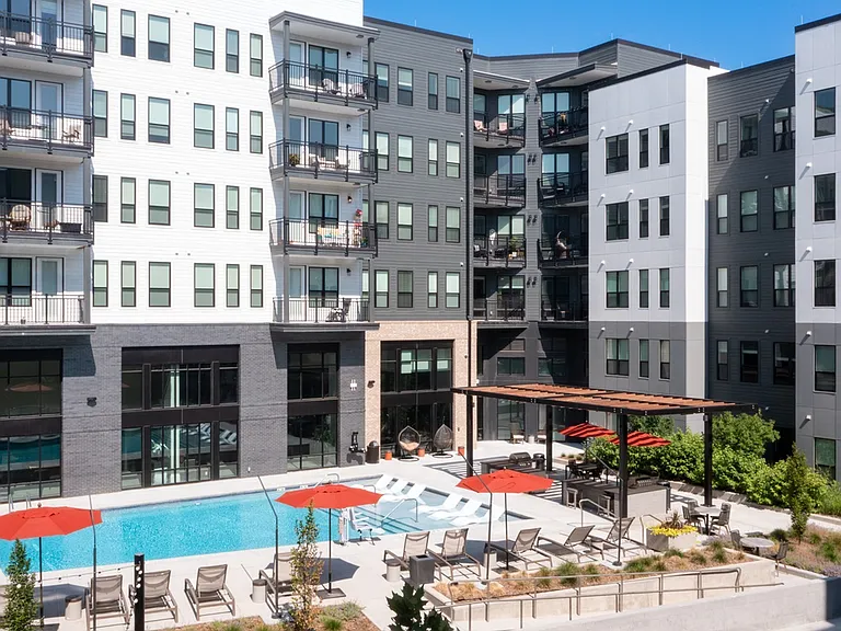 A vibrant retreat featuring a resort-style pool, plush loungers, red umbrellas, and lush landscaping_right outside your door.